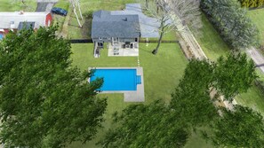 An aerial view of a house with a swimming pool, surrounded by trees and a fenced yard.