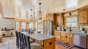 A spacious kitchen with wooden cabinets, a large island with bar stools, and a stainless steel refrigerator.