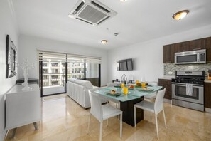 Une cuisine moderne avec un coin repas, comprenant une table en verre, des chaises blanches et une vue sur l’extérieur.