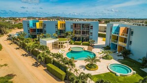 A modern hotel with multiple colorful buildings, a central swimming pool, and well-maintained gardens.