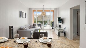 A modern living room with a dining area, a grey sofa, a coffee table, and a TV mounted on the wall.