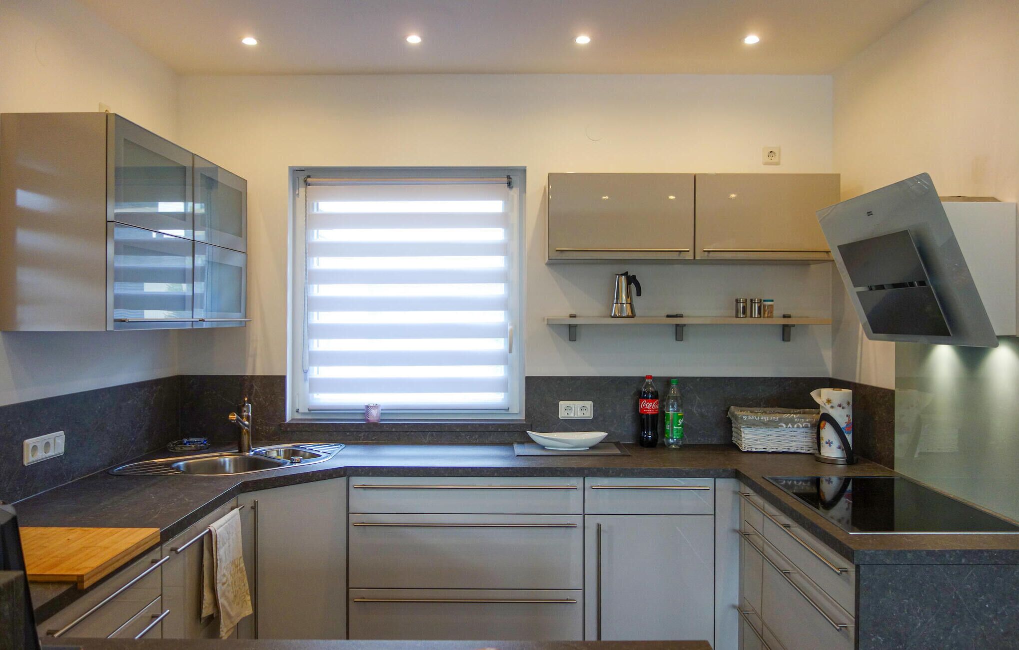 Een moderne keuken met een inbouwoven, een spoelbak en een raam met zonwering.