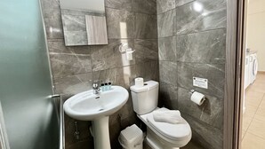 A modern bathroom with a pedestal sink, toilet, and a small trash bin. - STAY Symphony Apartment (Protaras)