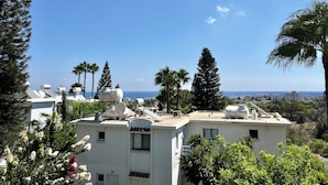 A residential area with multiple buildings, some with satellite dishes, surrounded by greenery and a clear view of the sea. - STAY Symphony Apartment (Protaras)
