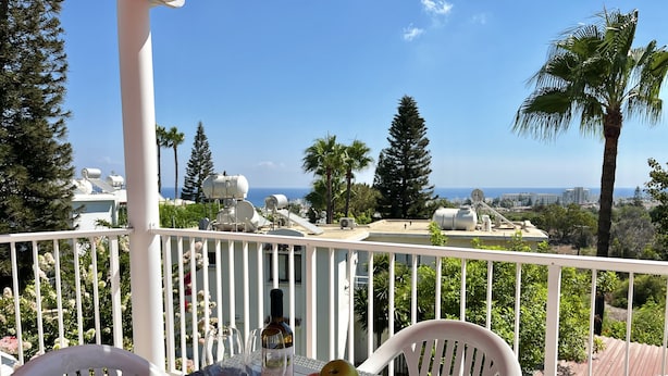 A balcony with a table set for two, featuring wine glasses, a bottle, and a fruit bowl. - STAY Symphony Apartment (Protaras)