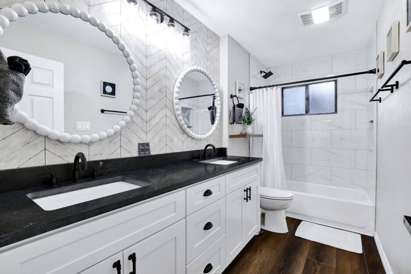 A modern bathroom with a black countertop, white cabinets, two sinks, a toilet, and a shower with a glass door.