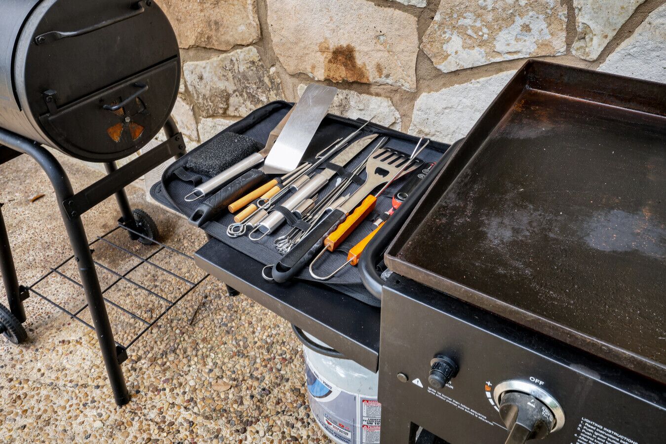 Ein tragbarer Grill mit einem Metalltablett, das verschiedene Utensilien und eine Propangasdose enthält.