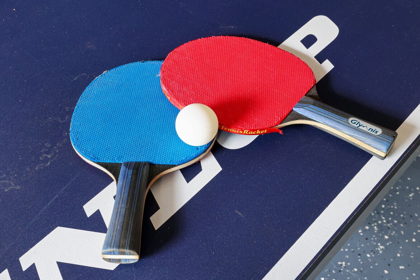 Two table tennis paddles with a white ball between them on a dark surface with white markings.