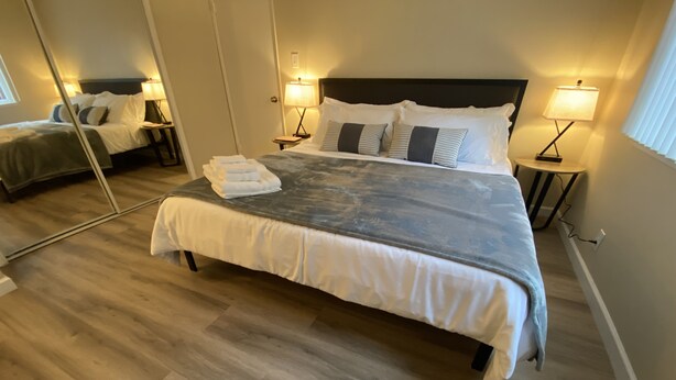 A hotel room with a large bed, two bedside tables with lamps, a mirror, and a wooden floor. - Cozy 1K & 1Q / 1b, 5 minutes walk to downtown (Lafayette)