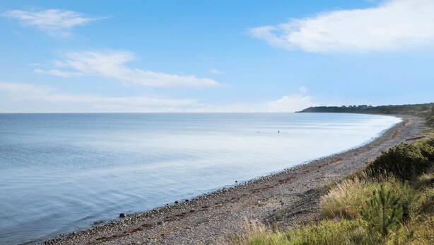 Ein Küstenstrand mit Kiesufer und blauem Himmel.