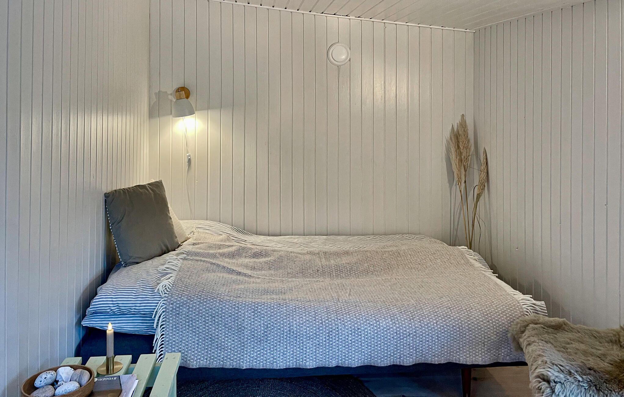 Ein Schlafzimmer mit einem Bett, einem Nachttisch mit Lampe, einer Zierpflanze und einer Wandleuchte.