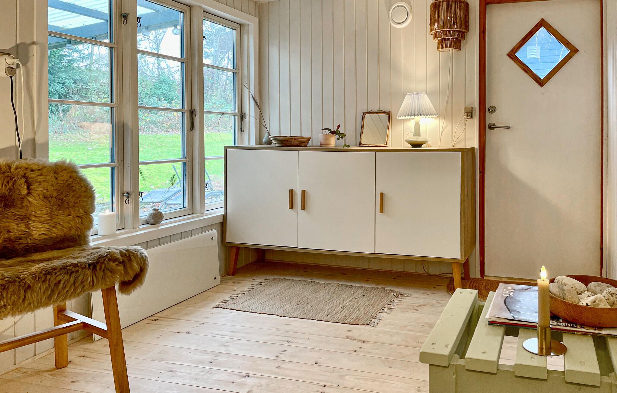 Een gezellige kamer met een houten vloer, een vachtstoel, een wit kastje en een deur met een klein raam.