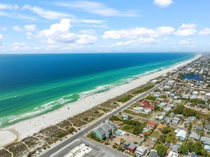 An aerial view of a coastal town with a beach, houses, and a road.