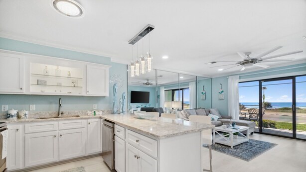 A modern kitchen with white cabinets, a central island, and a dining area with a view of the ocean. - LAGUNA DUNES! AMAZING VIEWS! GROUND FLOOR! (Panama City Beach)