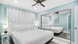 A bedroom with a bed, a nightstand, a mirror, a ceiling fan, and a window with curtains. - LAGUNA DUNES! AMAZING VIEWS! GROUND FLOOR! (Panama City Beach)