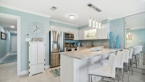 A modern kitchen with white cabinetry, stainless steel appliances, and a central island with bar stools. - LAGUNA DUNES! AMAZING VIEWS! GROUND FLOOR! (Panama City Beach)