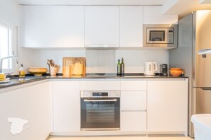 Une cuisine moderne avec des meubles blancs, un four encastré, un four à micro-ondes et une machine à café.