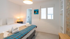 Ein Schlafzimmer mit einem Bett, einem Nachttisch mit Lampe, einem Fenster und einer Tür.