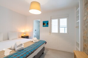 Ein Schlafzimmer mit einem Bett, einem Nachttisch mit Lampe, einem Fenster und einer Tür.