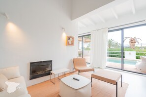 Ein modernes Wohnzimmer mit Kamin, Sitzgruppe und Blick auf einen Pool.