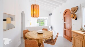 Un coin repas avec une table ronde, des chaises en osier, un luminaire suspendu et une porte en bois.