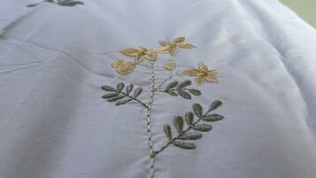 A bed with a white bedspread featuring embroidered floral designs.