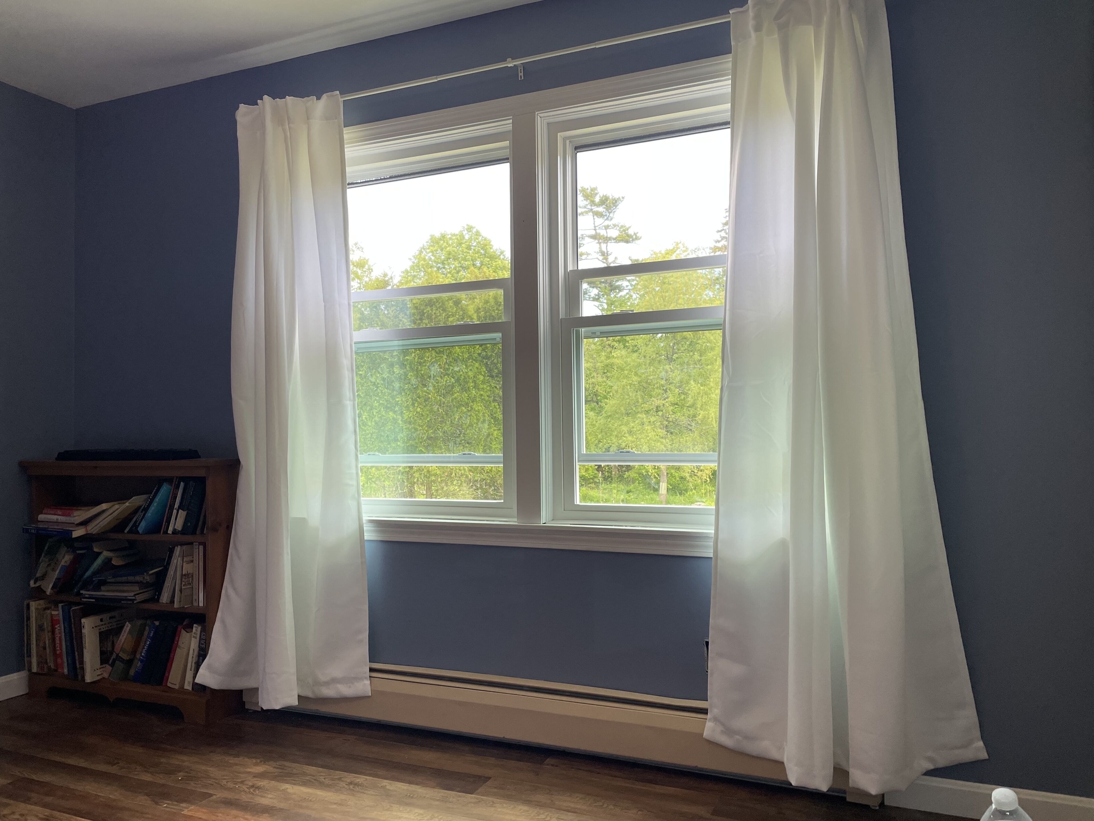 A room with a large window, a wooden bookshelf, and a radiator.