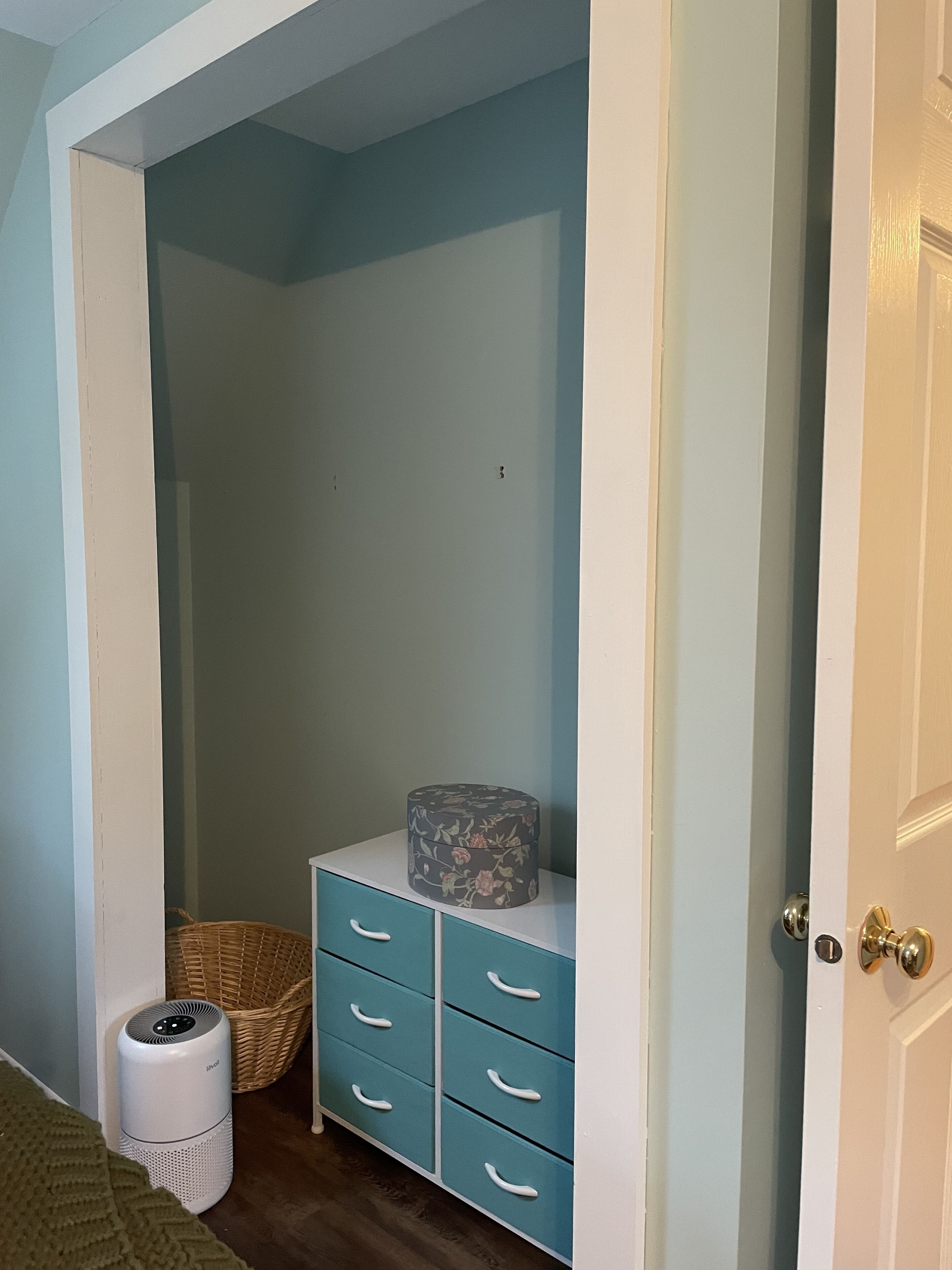 A room with a blue wall, a white door, a white ceiling, and a white floor. There is a white trash can and a wicker basket.