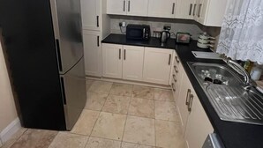 A compact kitchen with white cabinets, a black refrigerator, a microwave, a kettle, and a washing machine. - Remarkable 3-Bed House in Westcliff-on-Sea (Westcliff-on-Sea)