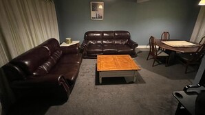 A living room with a dark brown leather sofa, a wooden coffee table, a dining table with chairs, and a hanging light fixture. - Remarkable 3-Bed House in Westcliff-on-Sea (Westcliff-on-Sea)