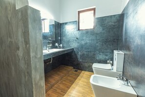 Ein modernes Badezimmer mit Holzboden, einem großen Spiegel, einem Waschbecken, einer Toilette und einer Badewanne.
