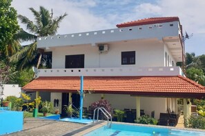 Ein zweistöckiges Gebäude mit Swimmingpool, einer überdachten Terrasse und einem roten Ziegeldach.