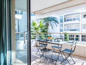 Varanda externa com mesa, cadeiras e vista para palmeiras e um edifício.