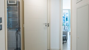 A modern, minimalist bathroom with a white door, a glass shower enclosure, and a visible towel rack.