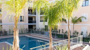 A swimming pool surrounded by palm trees and a multi-story building with balconies.