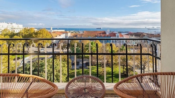 Un balcon avec des fauteuils en osier, une vue sur le paysage urbain de la côte et un ciel dégagé.
