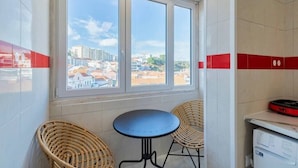 Une pièce avec une grande fenêtre, deux fauteuils en osier, une petite table ronde et une imprimante posée sur une étagère.