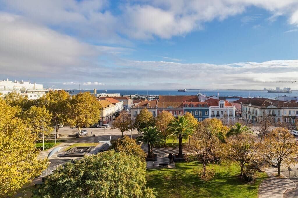 Paisagem costeira com edifícios históricos, um porto de recreio e vista clara para o mar.