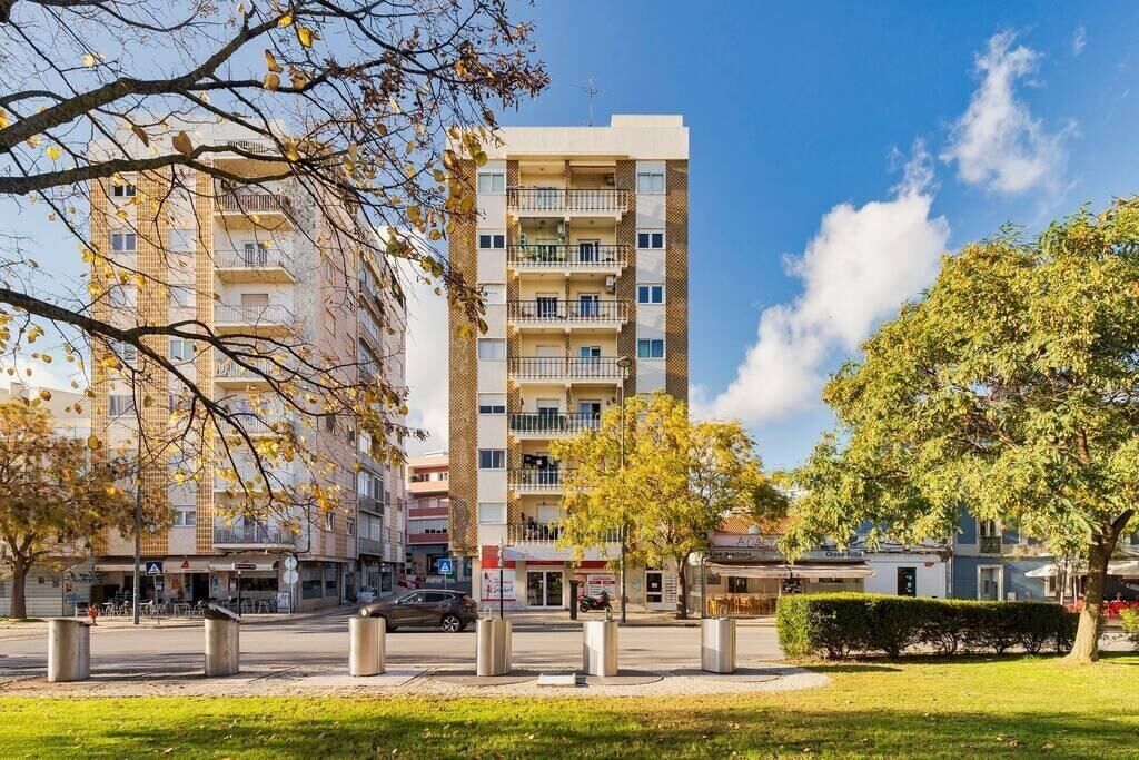 Um edifício residencial com vários andares, varandas, área gramada na frente e céu limpo.