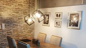 Un coin repas avec une table en bois, quatre chaises, un luminaire suspendu moderne et des tableaux encadrés au mur.