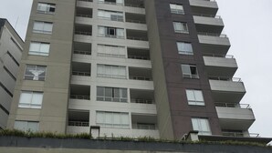 Un immeuble résidentiel à plusieurs étages, doté de balcons, d’une échelle de secours visible et d’une entrée fermée par un portail.