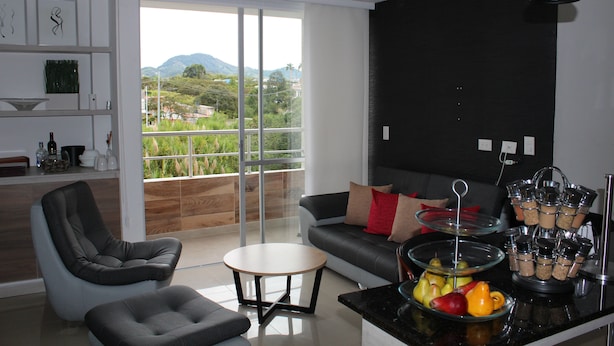 Un salon moderne avec un canapé, un fauteuil et une table basse. Une grande fenêtre offre une vue sur la verdure et les montagnes.