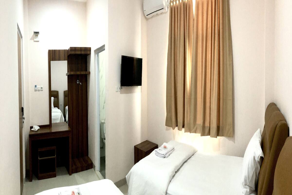 A hotel room with two beds, a TV, an air conditioning unit, a mirror, and a wooden dresser.