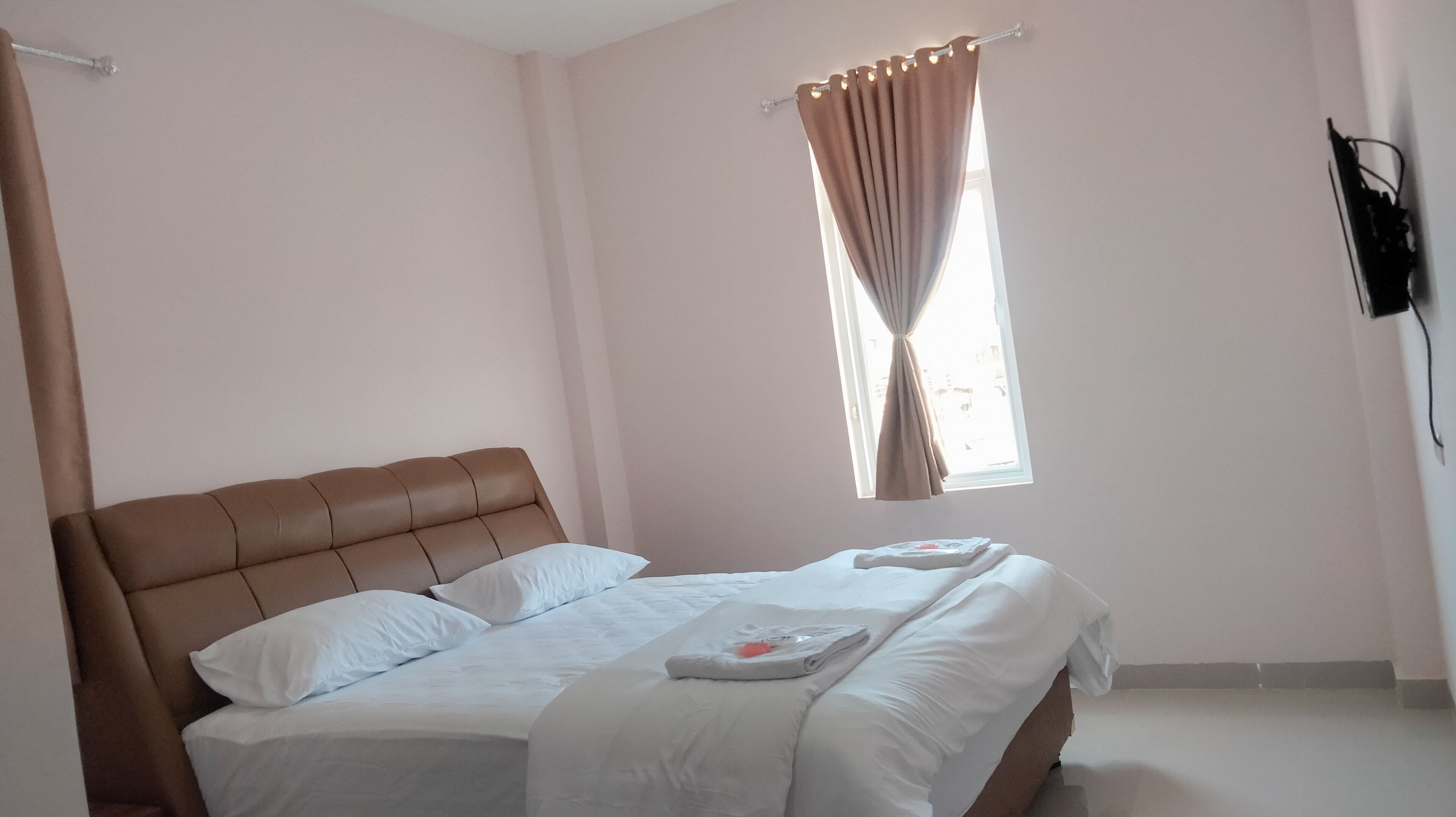 A bedroom with a bed, curtains, and a TV.
