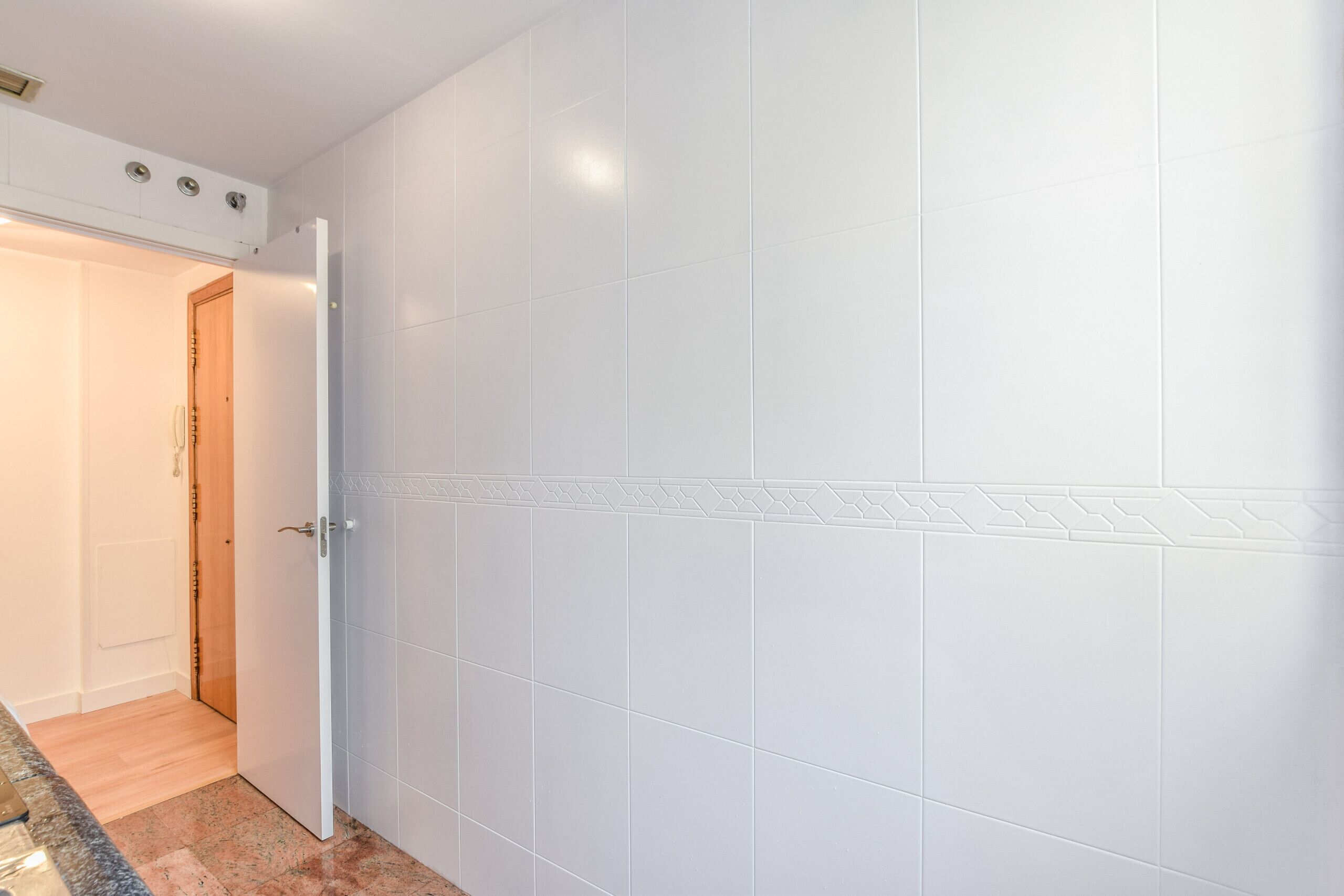 A closed door with a geometric pattern on the lower half, a wooden floor, and a white wall.