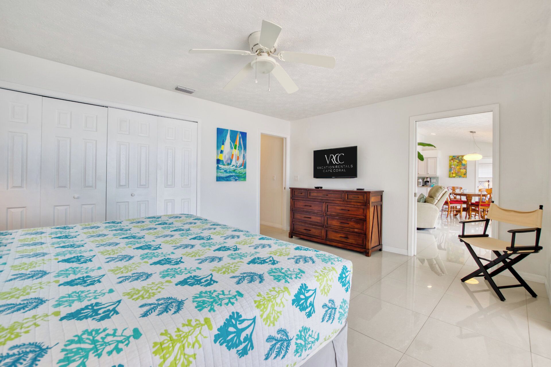 A bedroom with a bed, a ceiling fan, a TV, and a dresser.