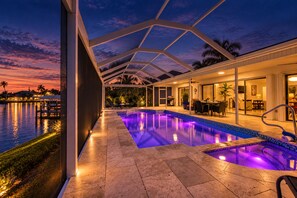 Une piscine entourée de parois en verre, un espace patio aménagé avec du mobilier d’extérieur et une vue sur l’eau.