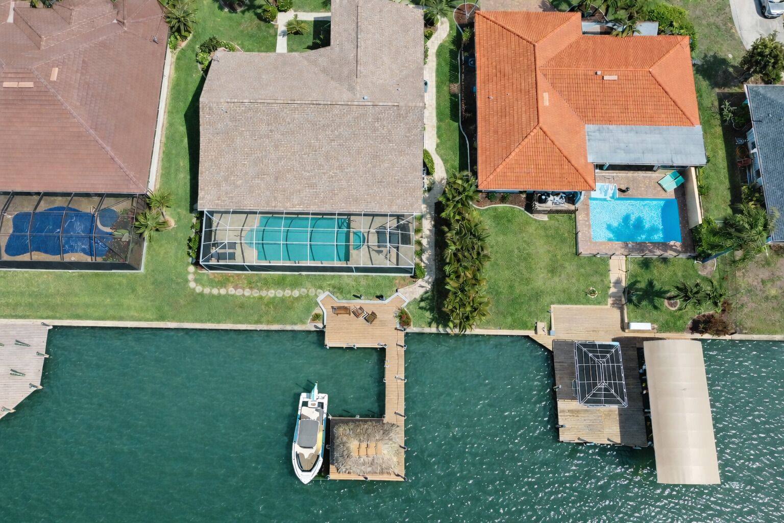 Vue aérienne d’une propriété comprenant une piscine, un quai avec un bateau et une grande maison avec un toit rouge.