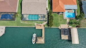 Vue aérienne d’une propriété comprenant une piscine, un quai avec un bateau et une grande maison avec un toit rouge.