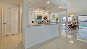 Une cuisine moderne avec des meubles blancs, un plan de travail en granit et un ventilateur de plafond.